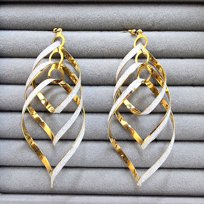 A pair of large dual-tone gold and silver glitter leaf-shaped dangling earrings on a grey velvet tray.