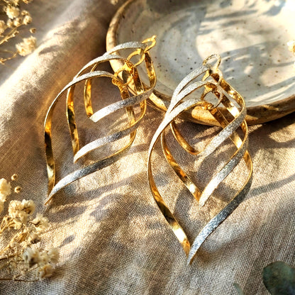 Aesthetic photography of sparkling multi-layered spiral earrings on linen fabric in warm sunlight.