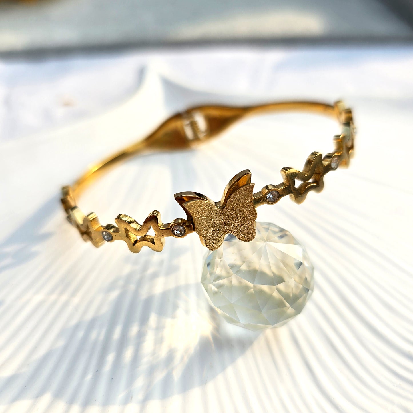 Gold hinged bangle featuring a textured stardust butterfly and crystal-studded star cutouts.