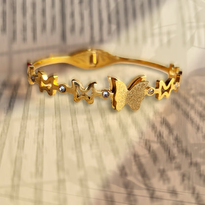 Close-up of matte finish gold butterfly charm on a celestial-themed bangle.