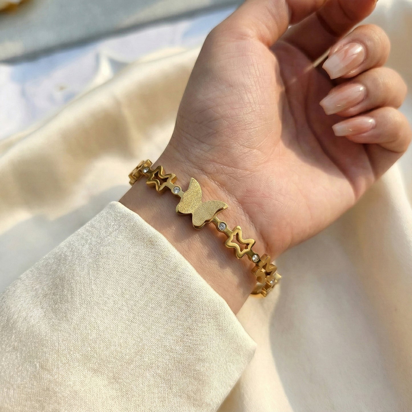 Woman wearing gold butterfly and star bangle styled with a soft cream sleeve.