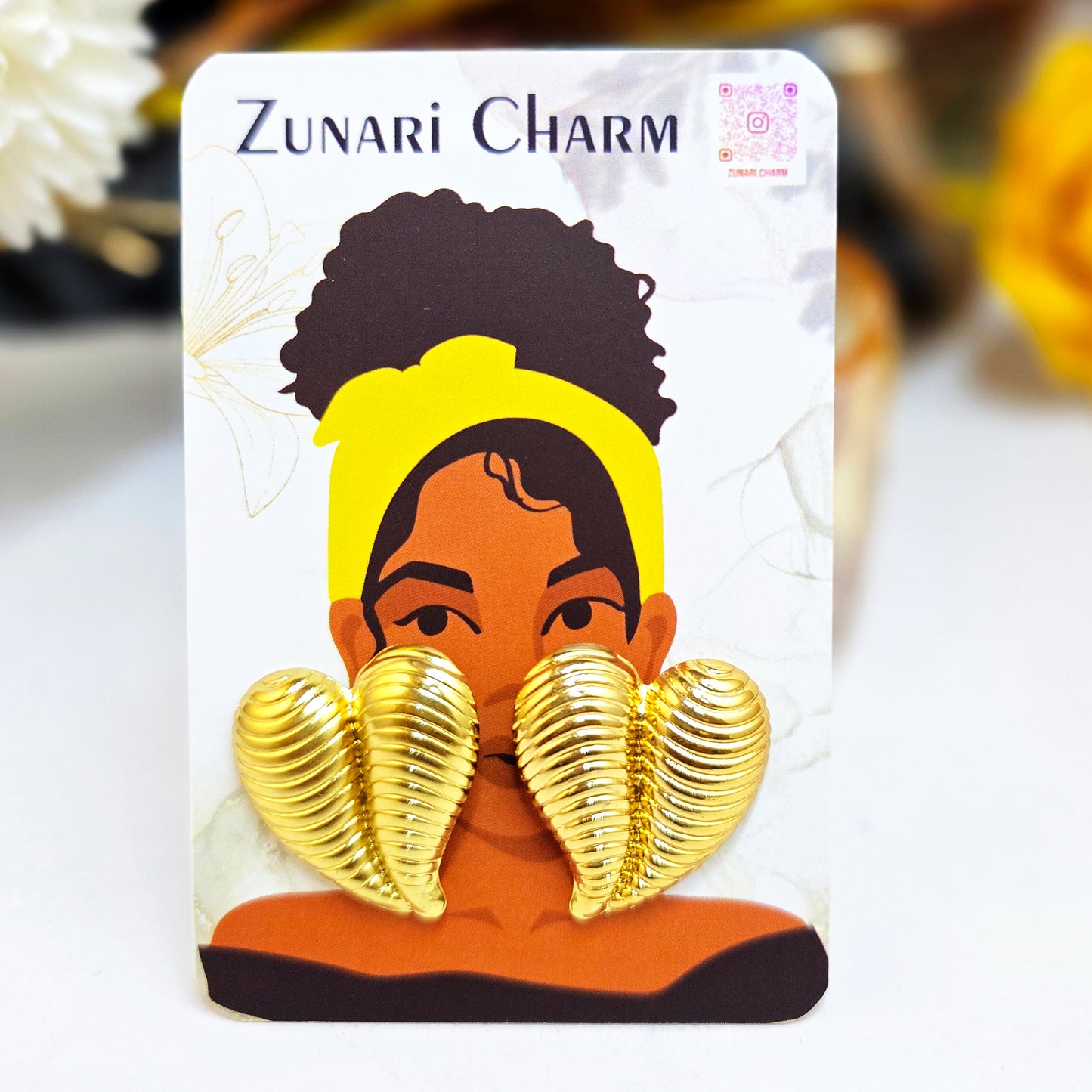 Striped gold heart earrings displayed on a Zunari Charm branded card featuring an illustrated woman with a yellow turban.