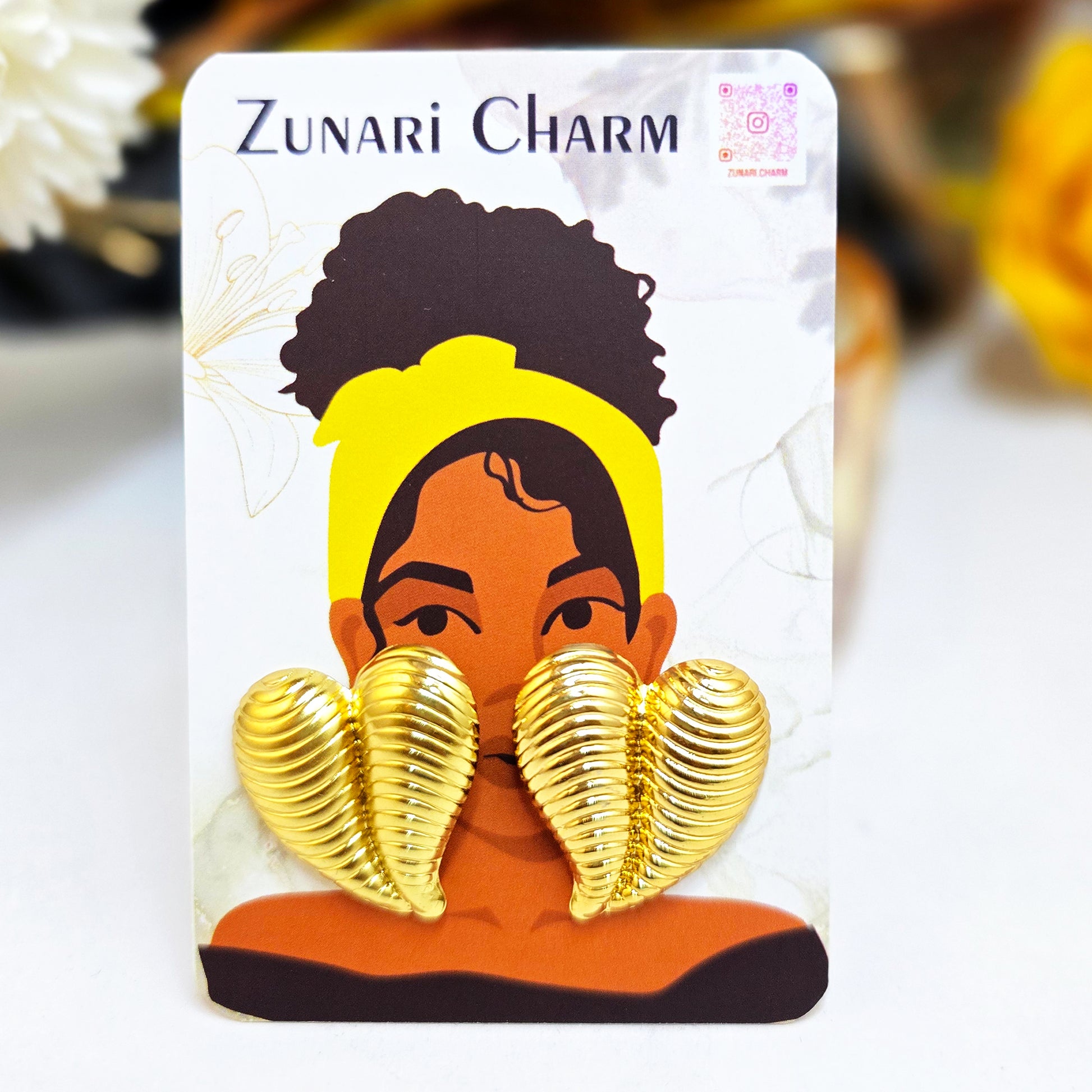 Striped gold heart earrings displayed on a Zunari Charm branded card featuring an illustrated woman with a yellow turban.