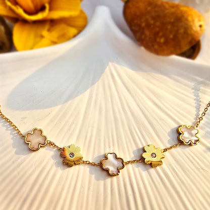 Flat lay of white enamel and gold textured flower bracelet on a white shell tray.