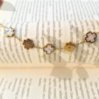 Gold bracelet with alternating white pearly clovers and textured sunburst charms draped on a book.