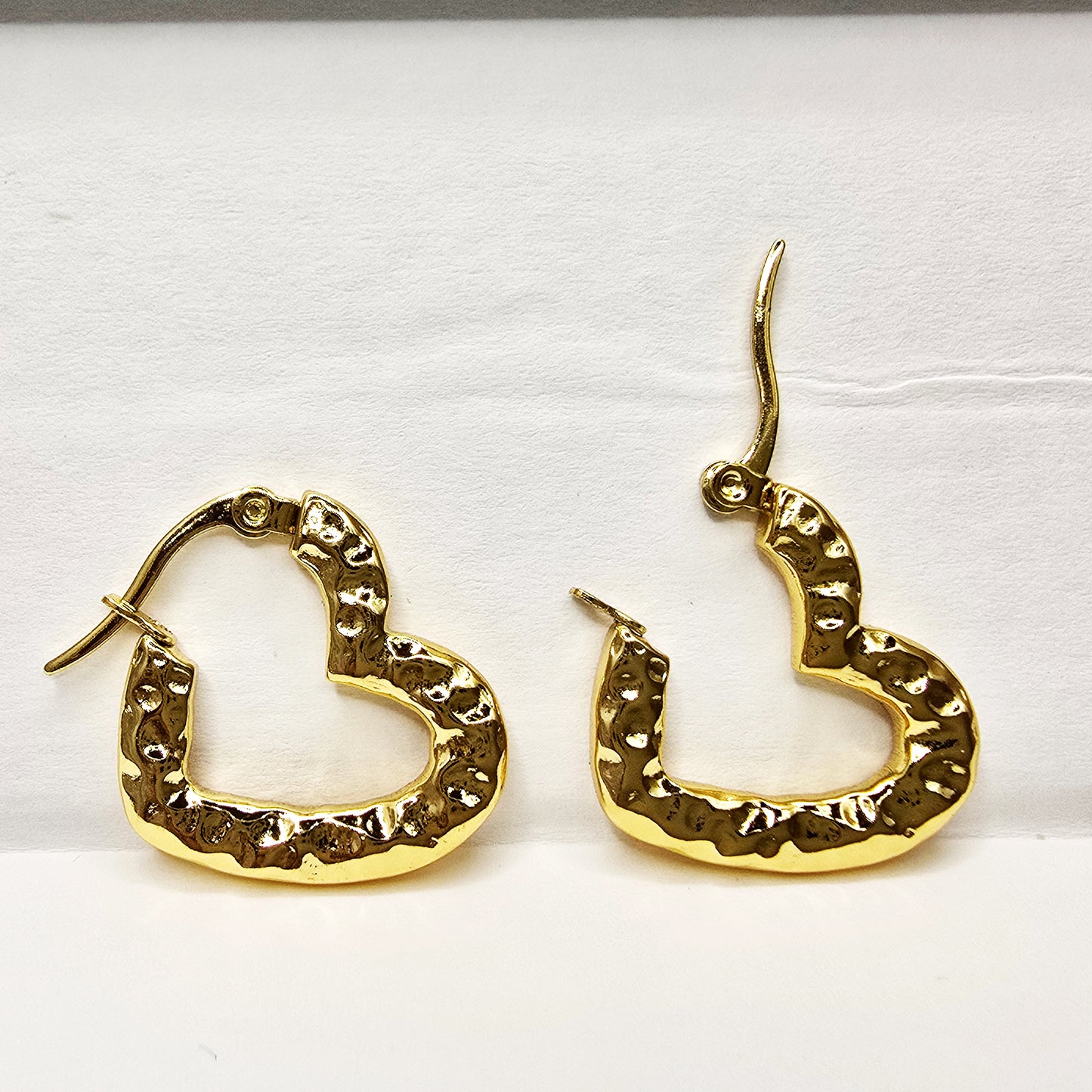 Pair of gold textured heart hoop earrings displayed flat on a white background.