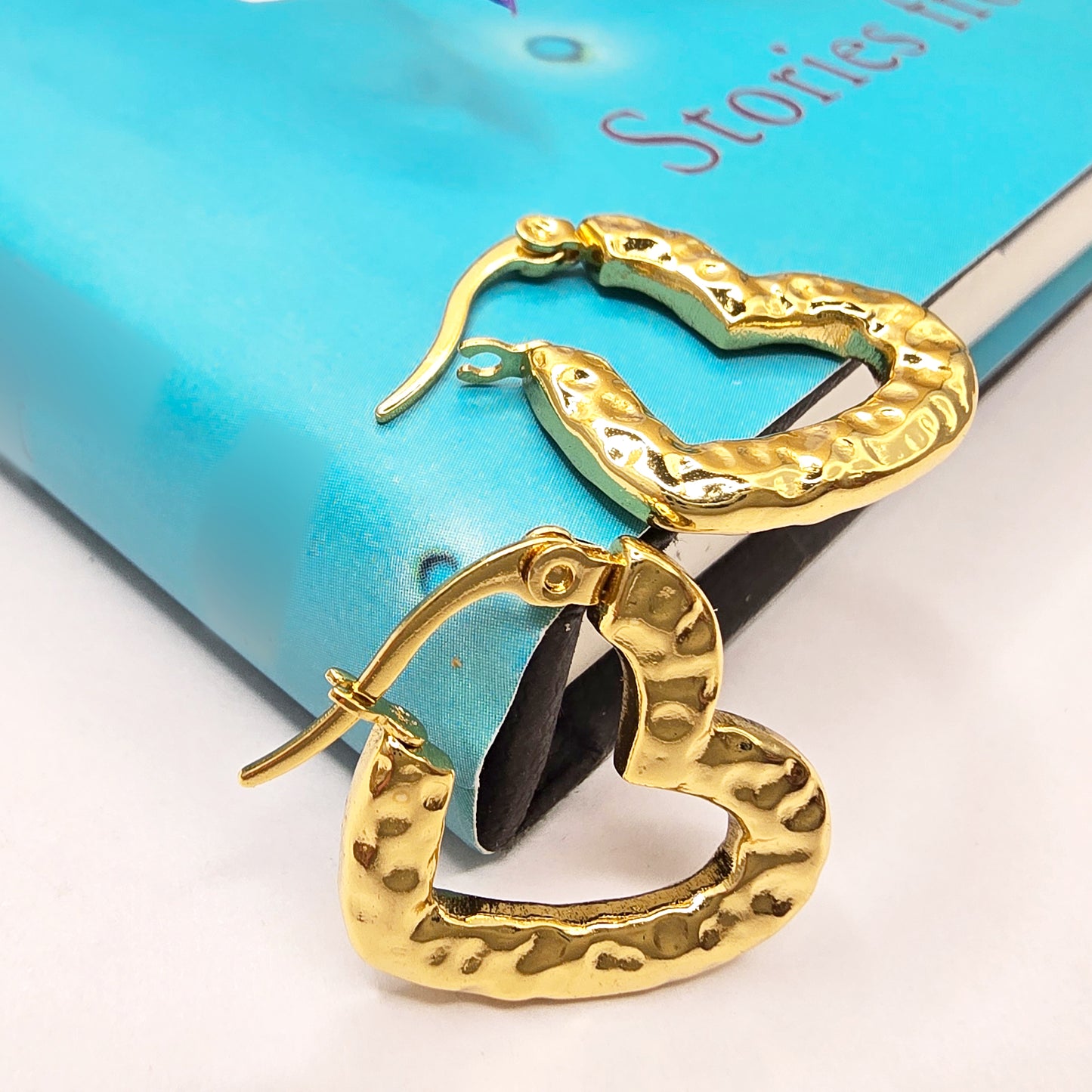 Gold textured heart hoop earrings placed on a blue book cover, showing hammered surface design.