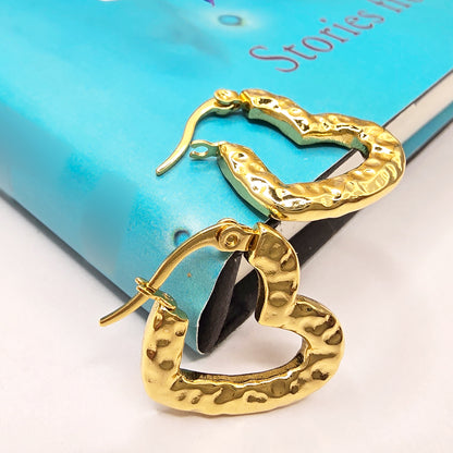 Gold textured heart hoop earrings placed on a blue book cover, showing hammered surface design.