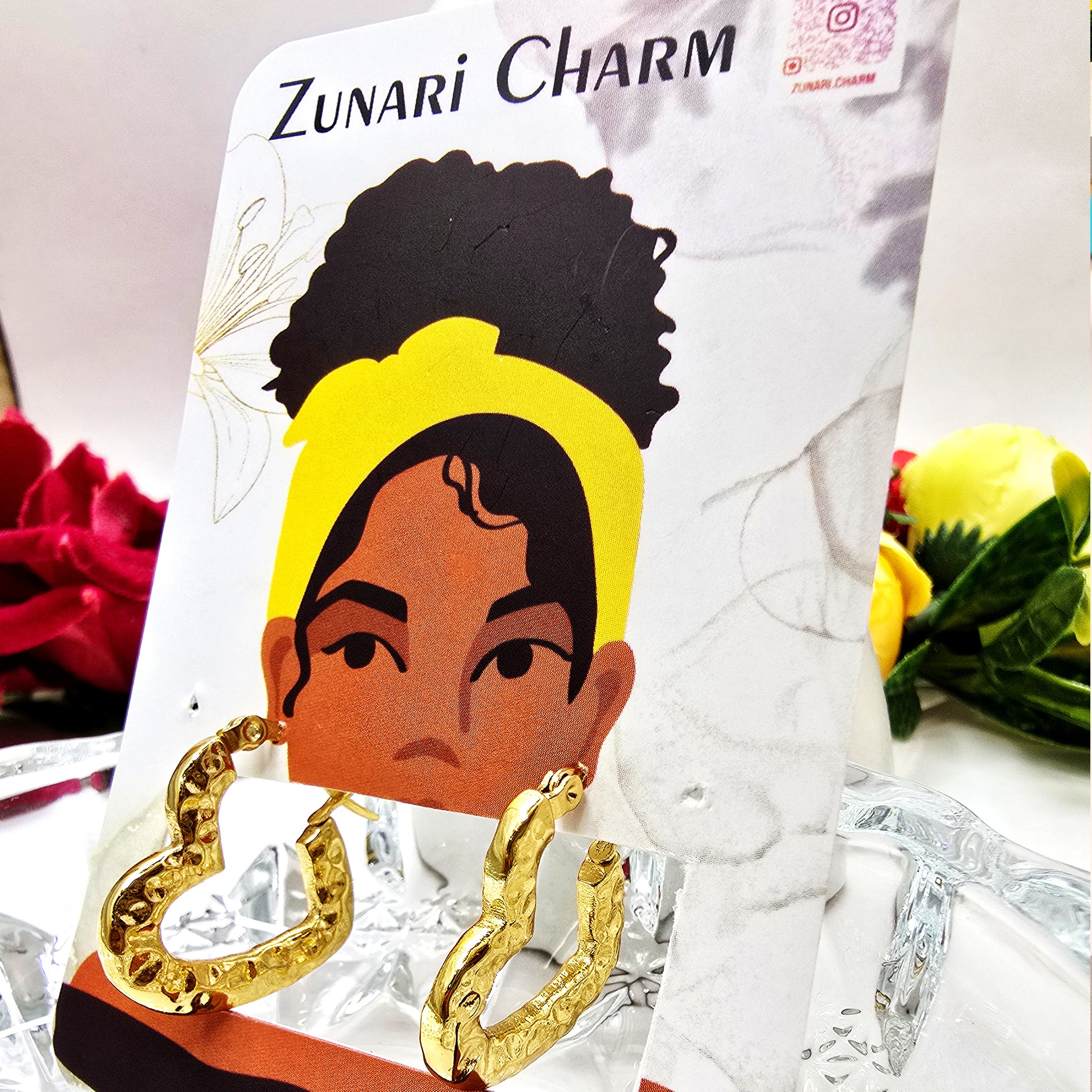Gold textured heart hoop earrings displayed on Zunari Charm branded jewelry card with floral and illustrated background.