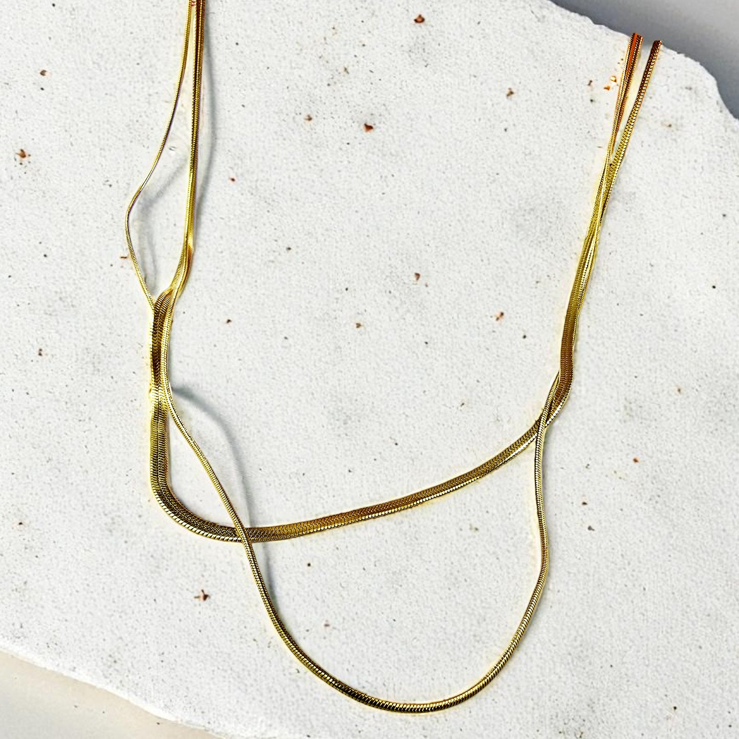 Flatlay of Trinity Layers Necklace on stone background – minimalist gold jewelry.