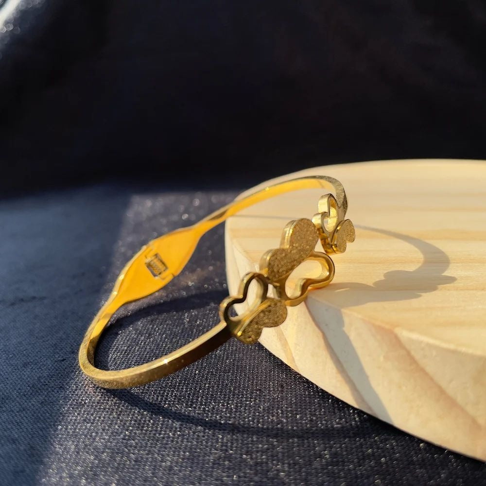 Triple Butterfly Bracelet in gold tone displayed on wooden base – angled view