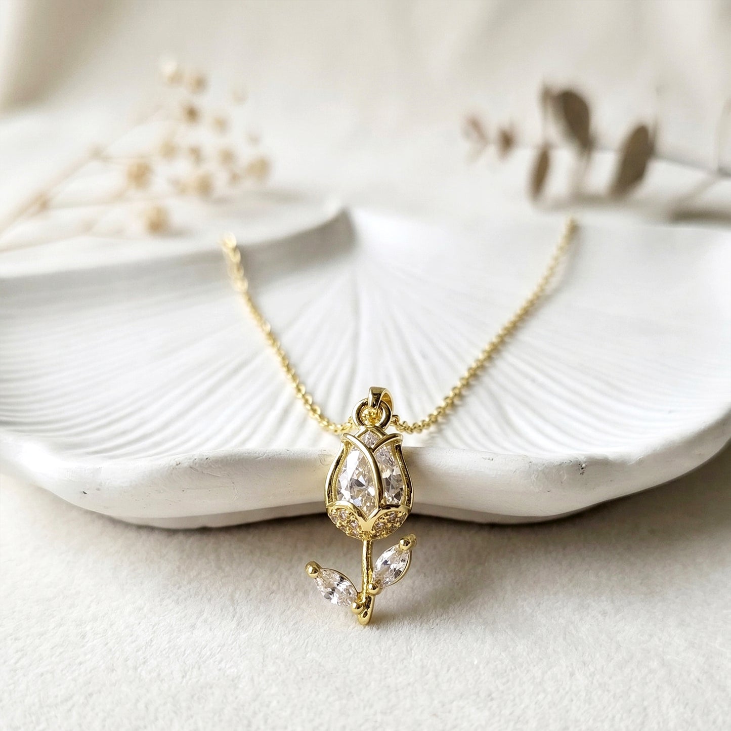 Elegant gold tulip pendant necklace with sparkling stones displayed on textured white leaf background