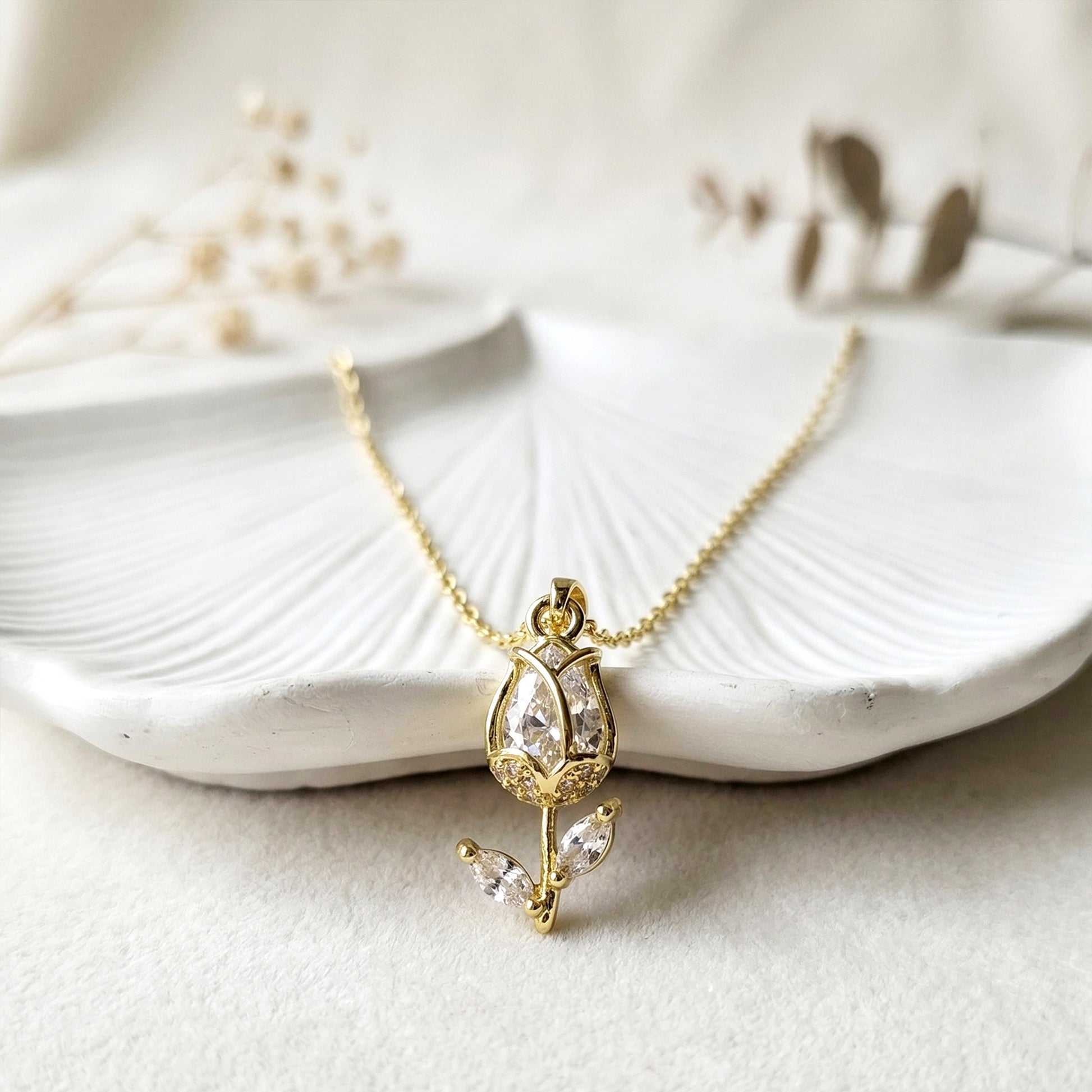 Elegant gold tulip pendant necklace with sparkling stones displayed on textured white leaf background