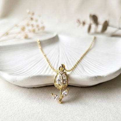 Elegant gold tulip pendant necklace with sparkling stones displayed on textured white leaf background