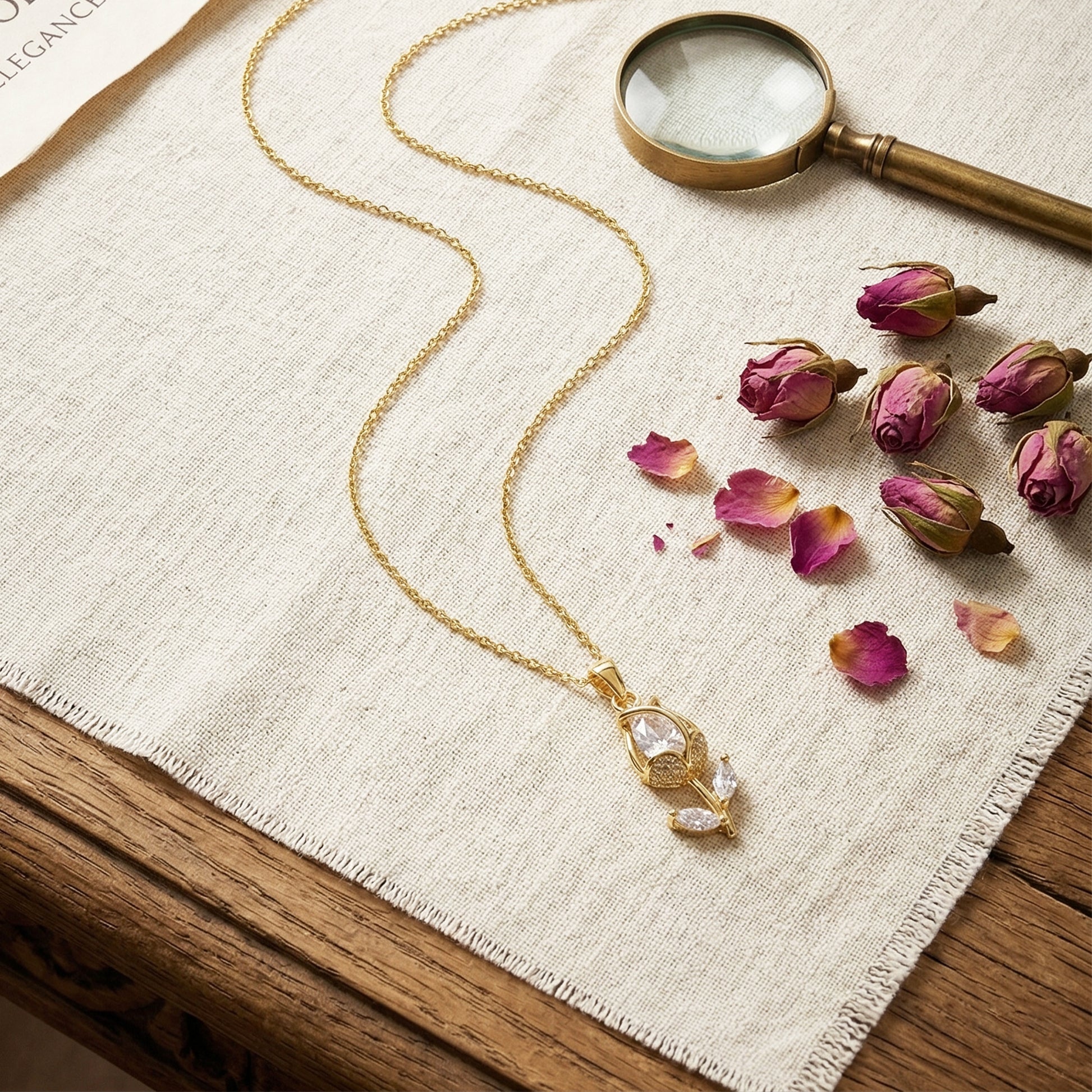 Gold tulip pendant necklace flatlay with dried roses and magnifier aesthetic luxury jewelry styling