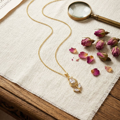 Gold tulip pendant necklace flatlay with dried roses and magnifier aesthetic luxury jewelry styling