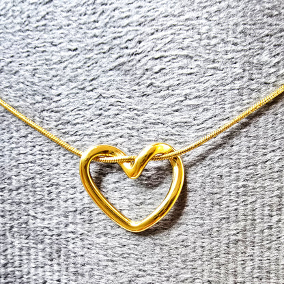 Close-up of the sculptural twisted open heart pendant and chain texture on a grey display.