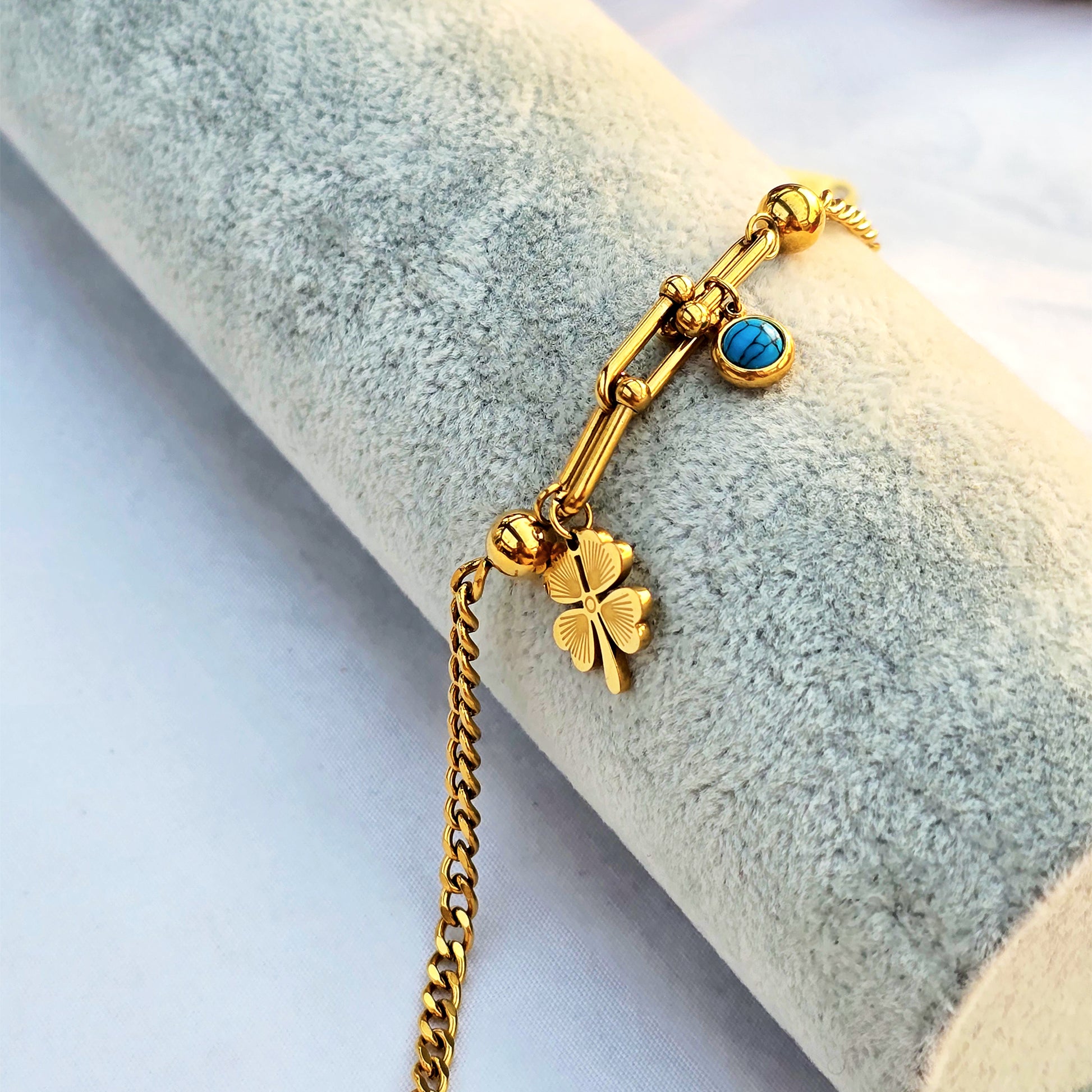 Studio shot of gold paperclip chain bracelet with a U-link connector and dangling black clover charm.