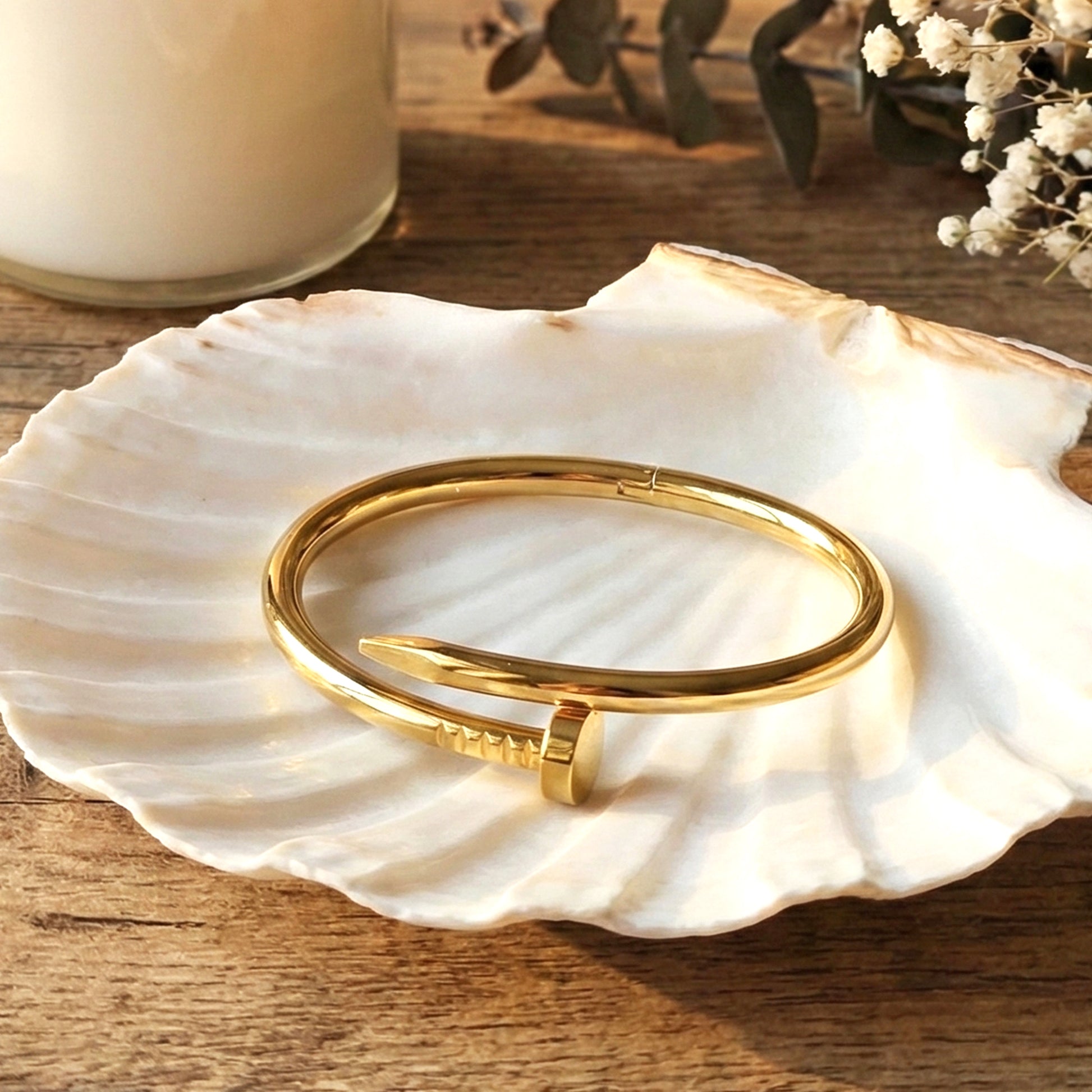 Minimalist gold nail cuff bracelet resting on a white shell tray.