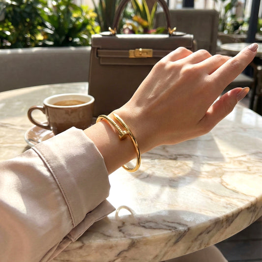 Woman's hand wearing gold nail-shaped bangle styled with luxury handbag and coffee.