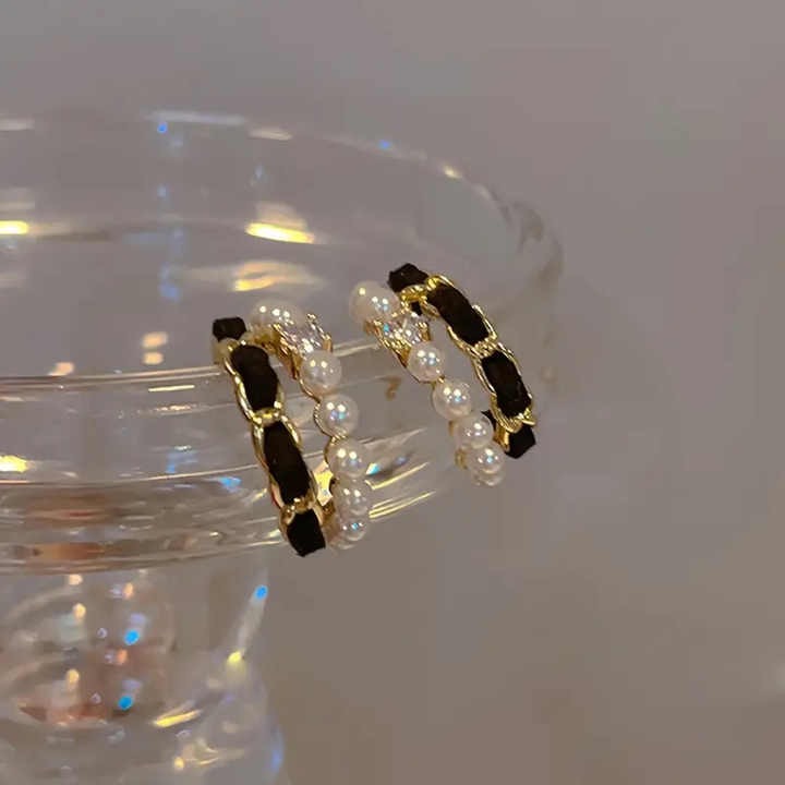 Elegant hoop earrings resting on glass rim – pearls, velvet, and gold chain