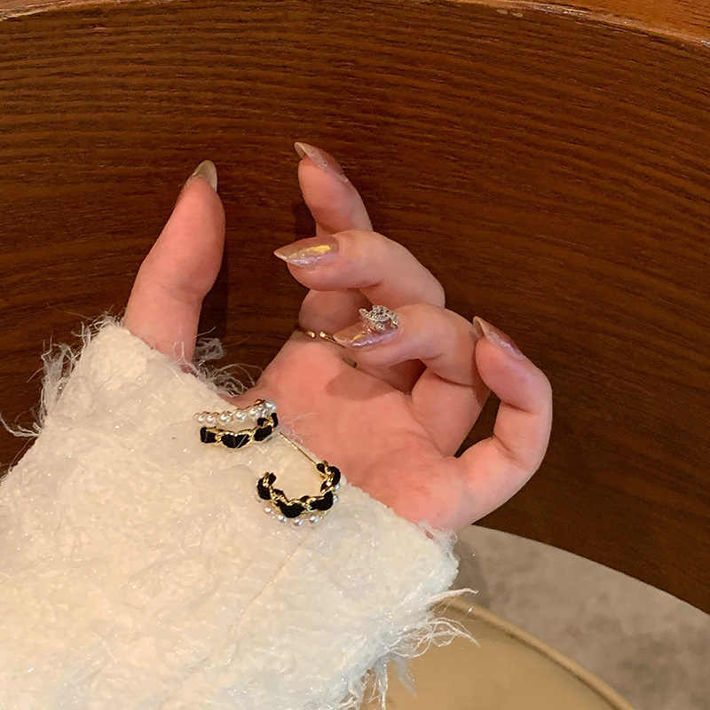 Model hand displaying chic black and gold pearl earrings with cozy sweater