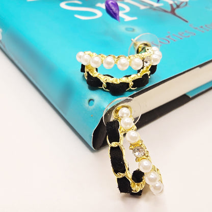 Gold hoop earrings with black velvet and pearls resting on a blue book
