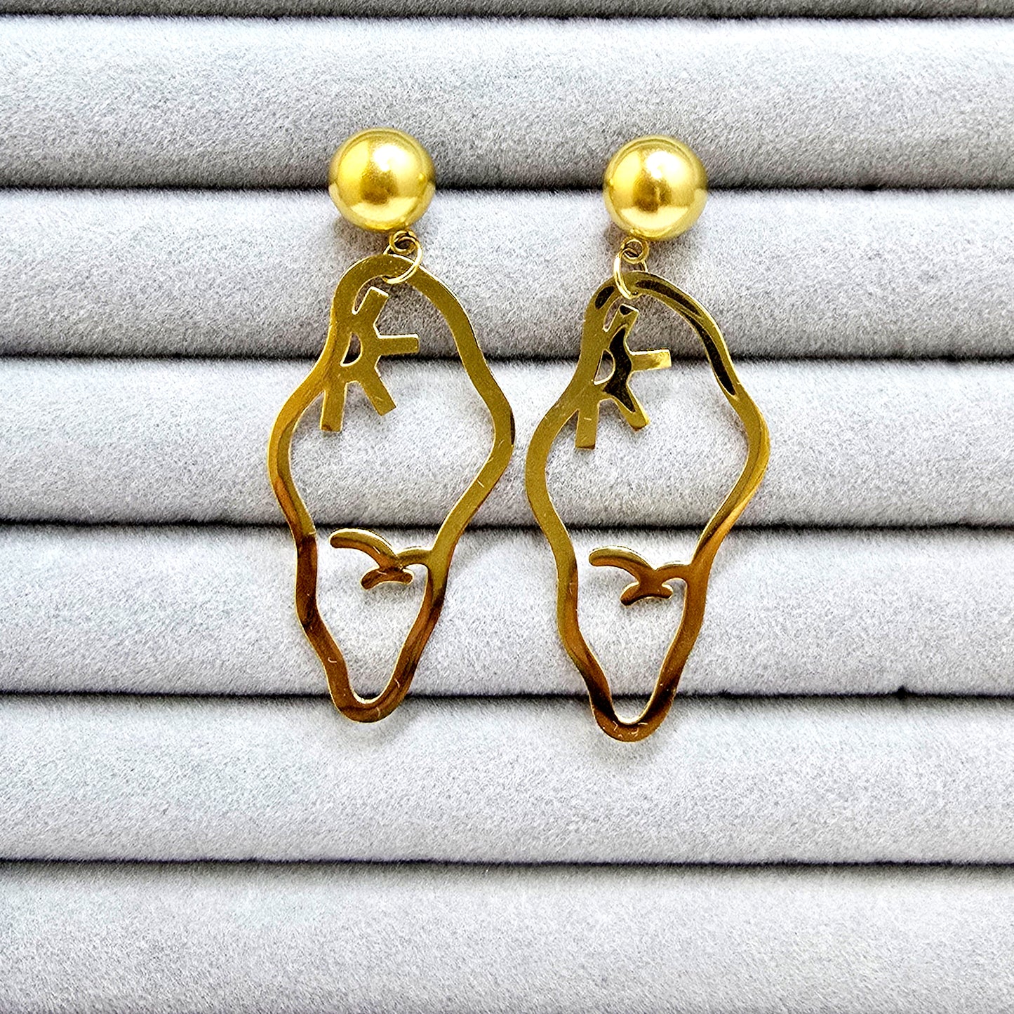 A pair of gold-plated Vertex earrings featuring a hollow-out bird and sun design on a grey velvet jewelry tray.