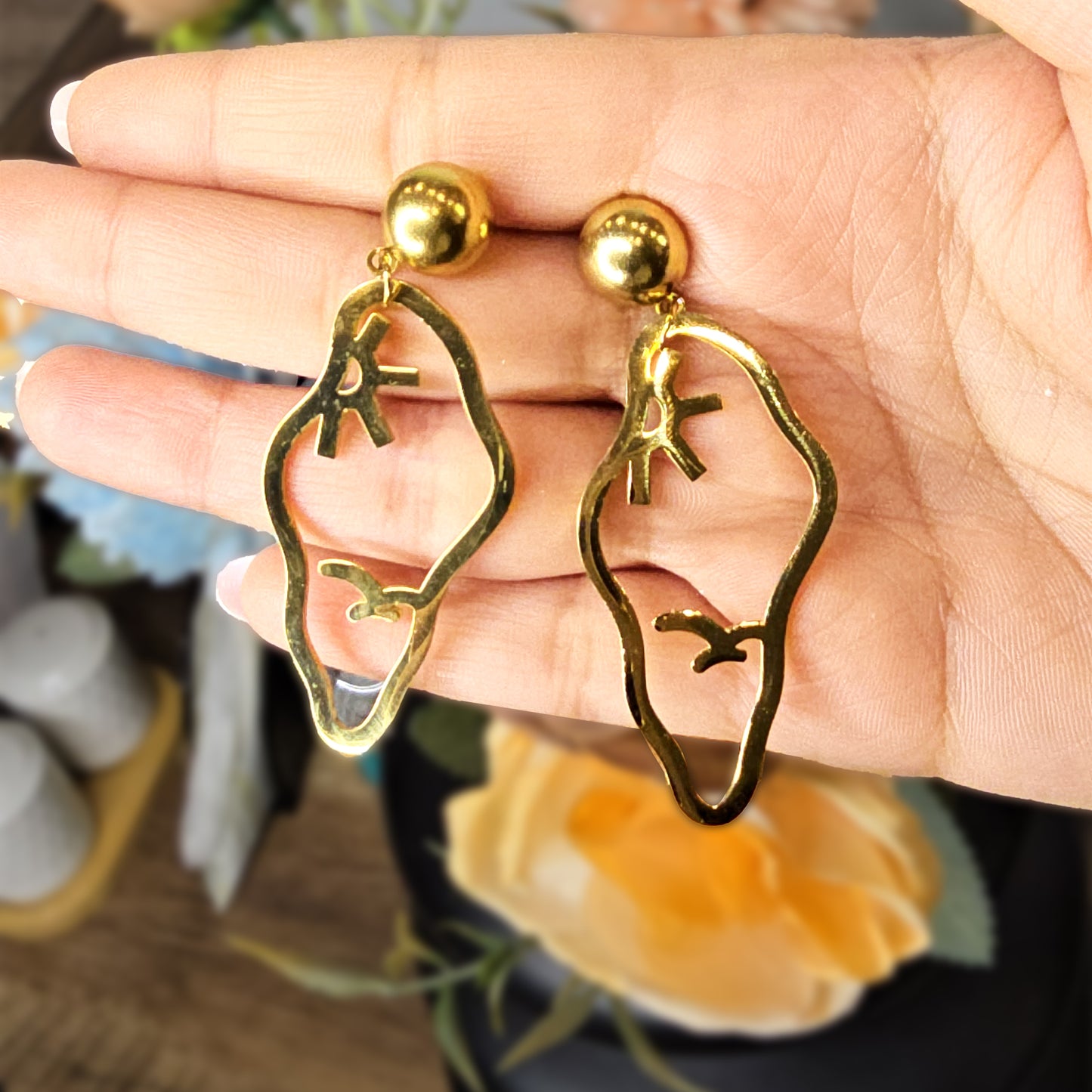 Hand holding large sculptural Vertex gold earrings to show the high-shine finish and intricate bird silhouette.