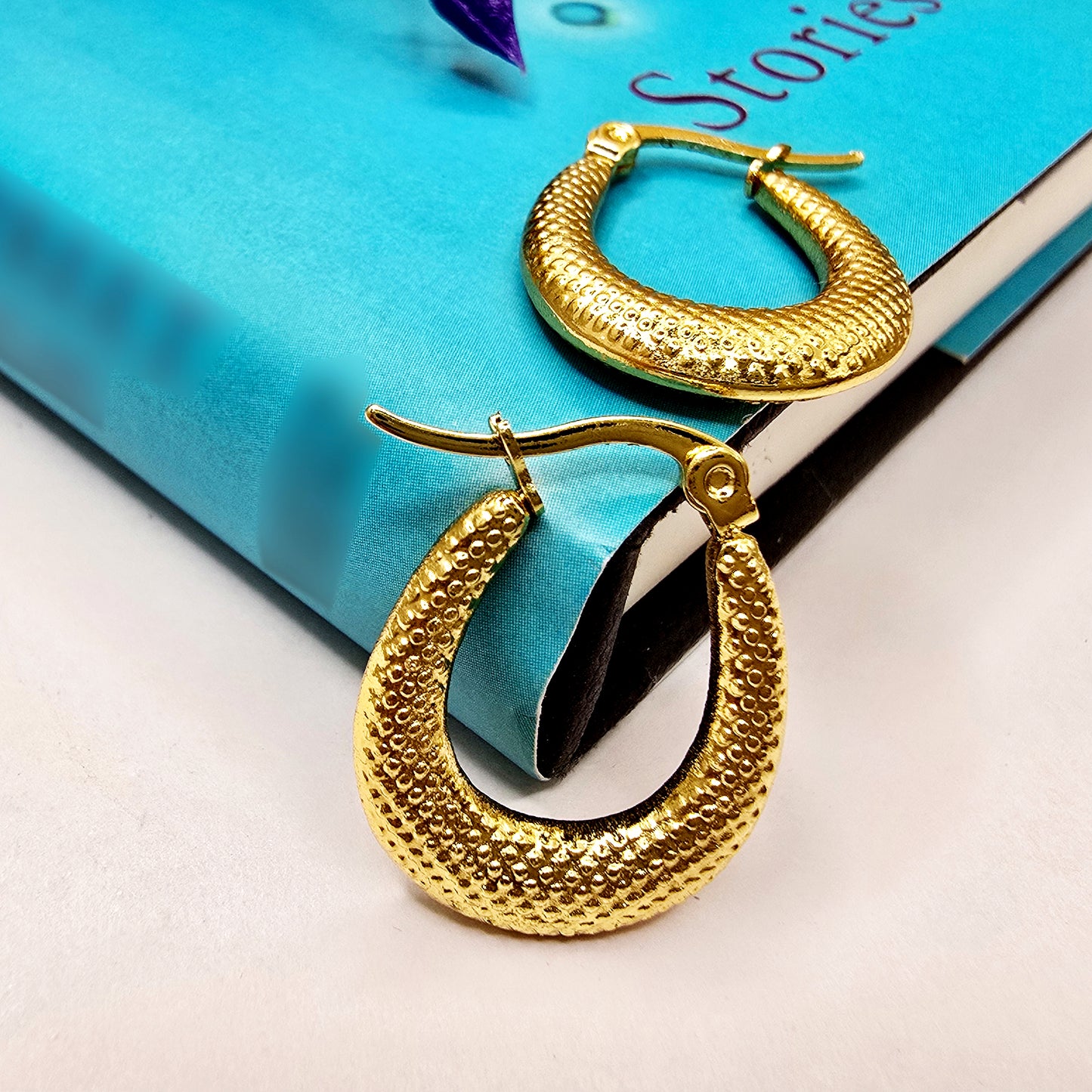 Gold crescent earrings displayed on a blue book, textured anti-tarnish finish