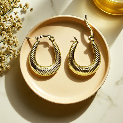 Crescent textured gold hoop earrings on ceramic plate with soft light