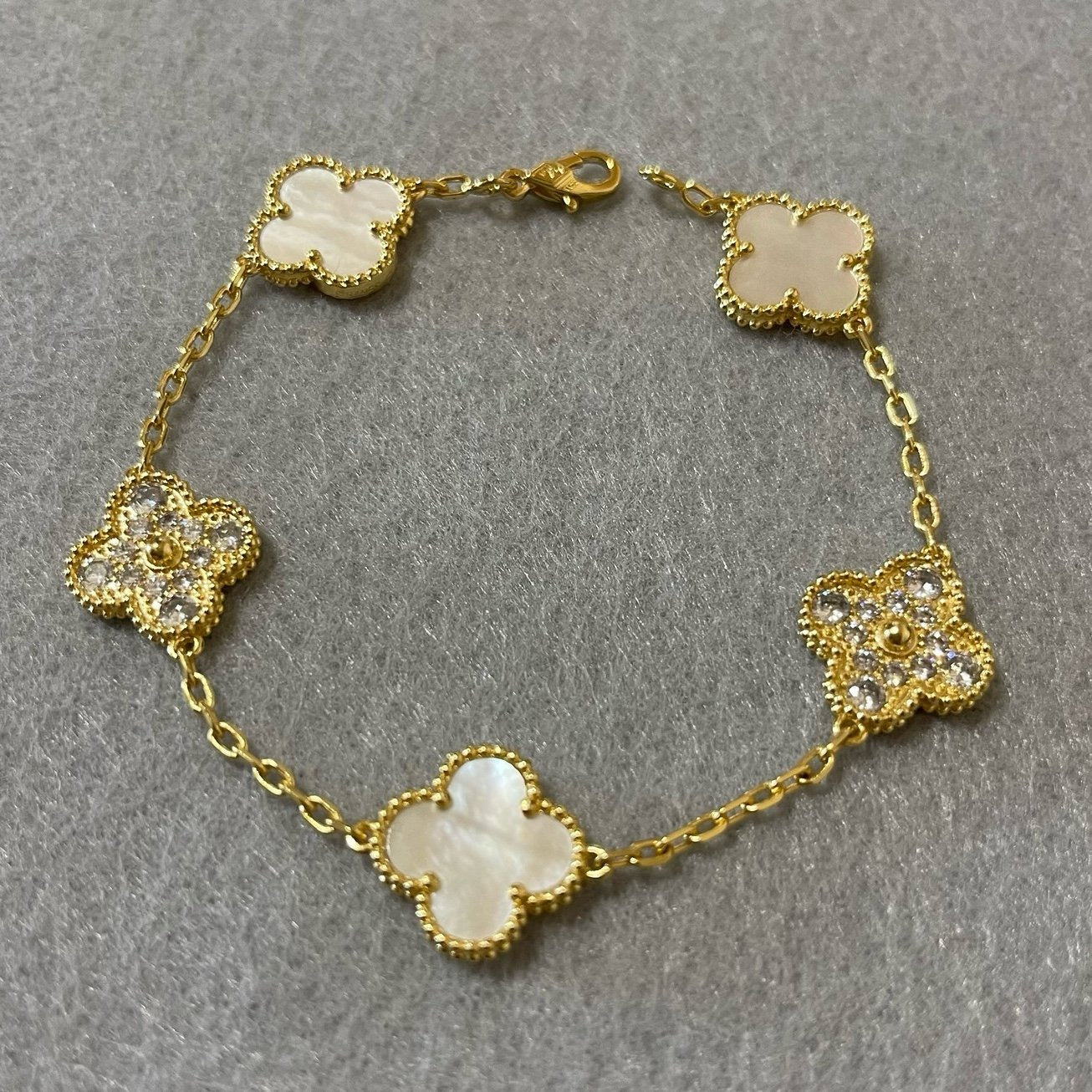 4-leaf clover gold charm bracelet laid flat on grey surface