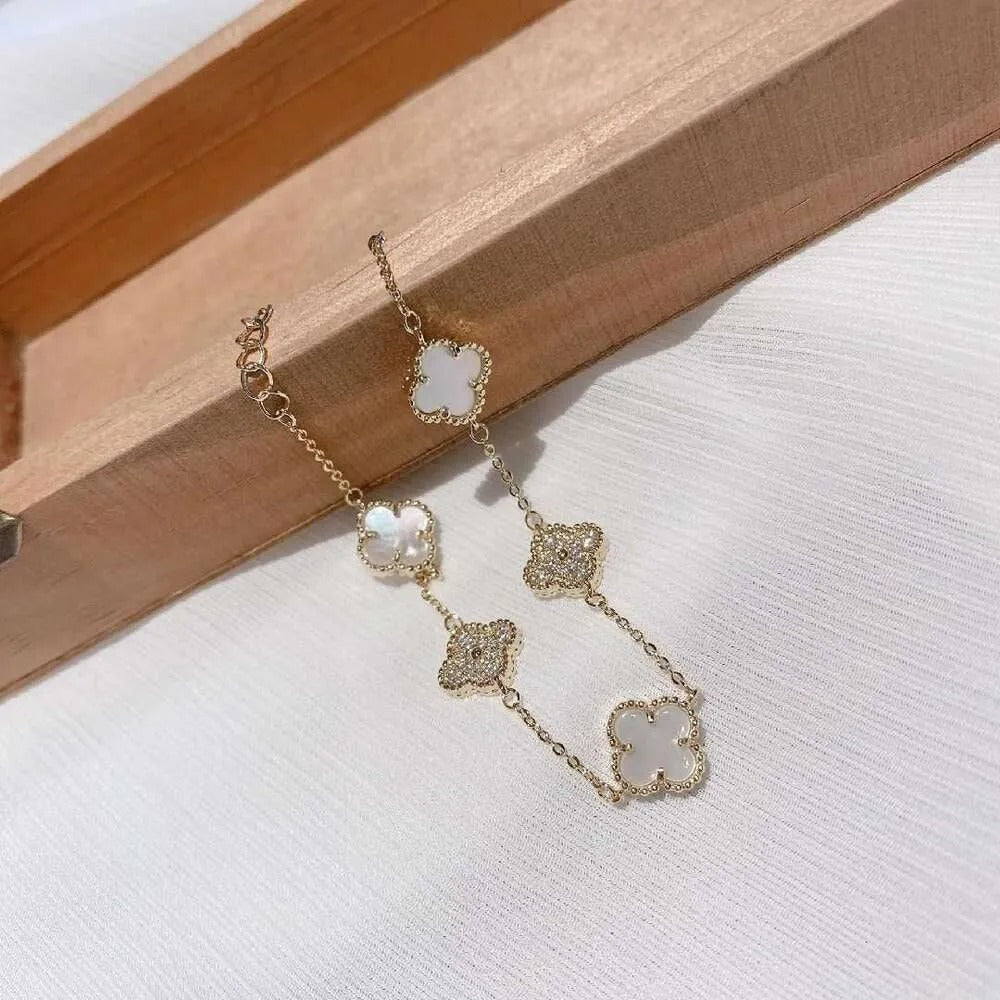 Bracelet with alternating white and crystal-studded clover charms near wooden box