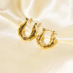 Glossy gold zigzag hoop earrings displayed on soft cream satin for an elegant and luxurious look