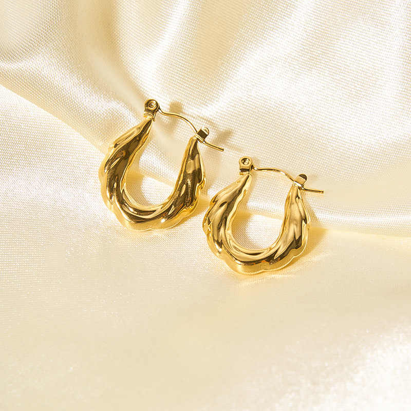 Glossy gold zigzag hoop earrings displayed on soft cream satin for an elegant and luxurious look