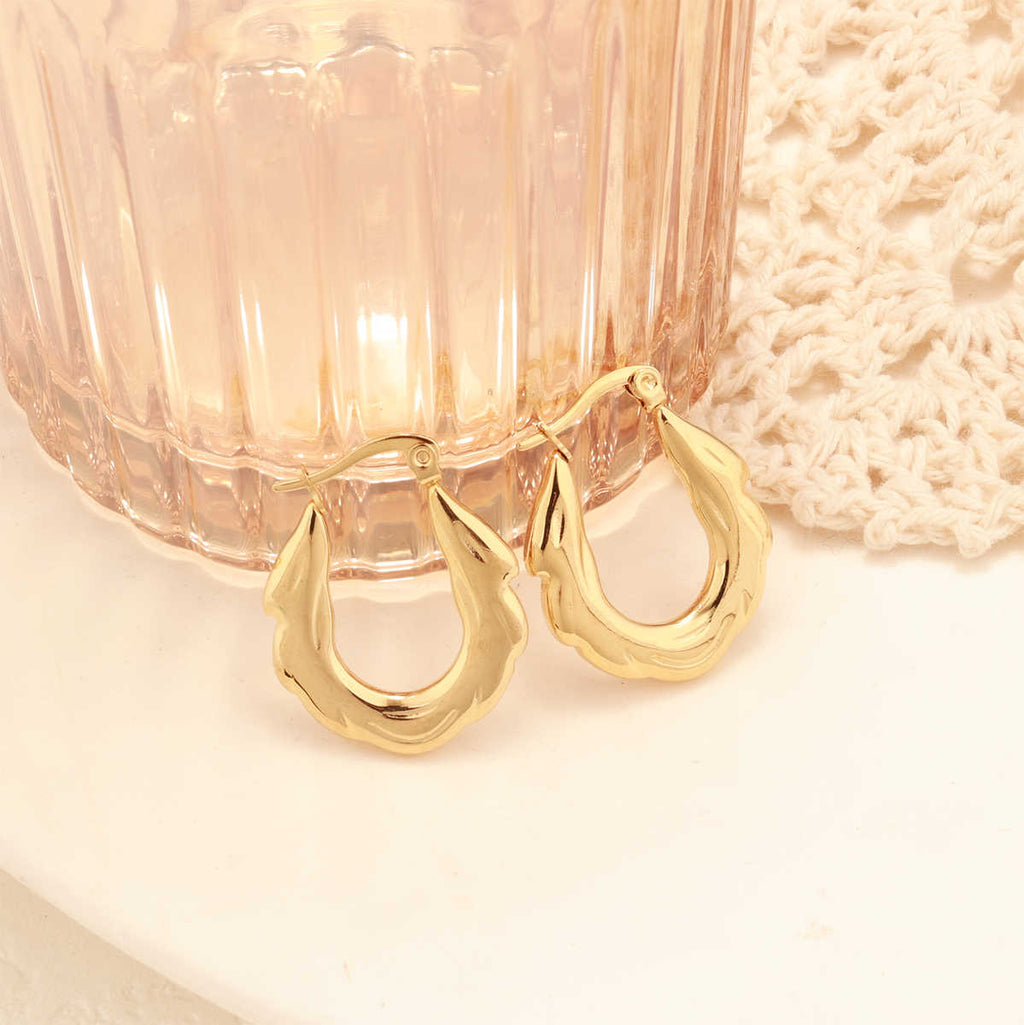 Close-up of gold zigzag hoop earrings placed on a round white ceramic tray with a blush glass and crochet decor.