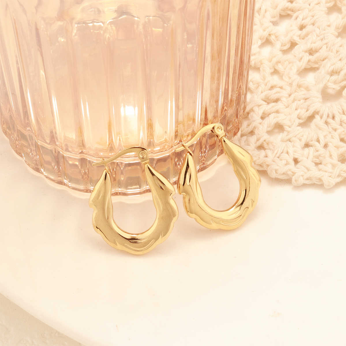 Close-up of gold zigzag hoop earrings placed on a round white ceramic tray with a blush glass and crochet decor.