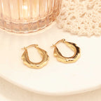 One gold zigzag hoop earring propped against a blush-toned glass with crochet detailing in background.