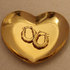 Pair of zigzag hoop earrings displayed in a heart-shaped golden dish on a beige fabric background.