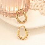 Gold zigzag hoop earrings placed beside a textured glass tumbler and lace fabric on a white ceramic plate