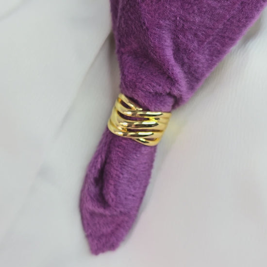 A 360-degree rotating video of the Ripple Band Ring, a gold-toned layered statement ring with wave-like ripples, displayed on a purple velvet background for an elegant showcase.