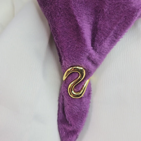 360-degree video of Zunari Charm Infinity Flow Ring on a rotating display table, featuring a bold sculptural gold design with fluid wave curves, shown against purple and white fabric backdrop.