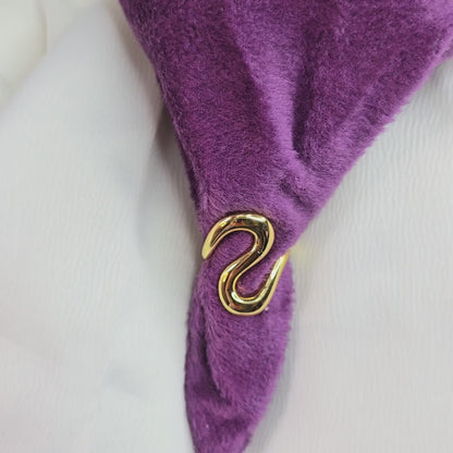 360-degree video of Zunari Charm Infinity Flow Ring on a rotating display table, featuring a bold sculptural gold design with fluid wave curves, shown against purple and white fabric backdrop.