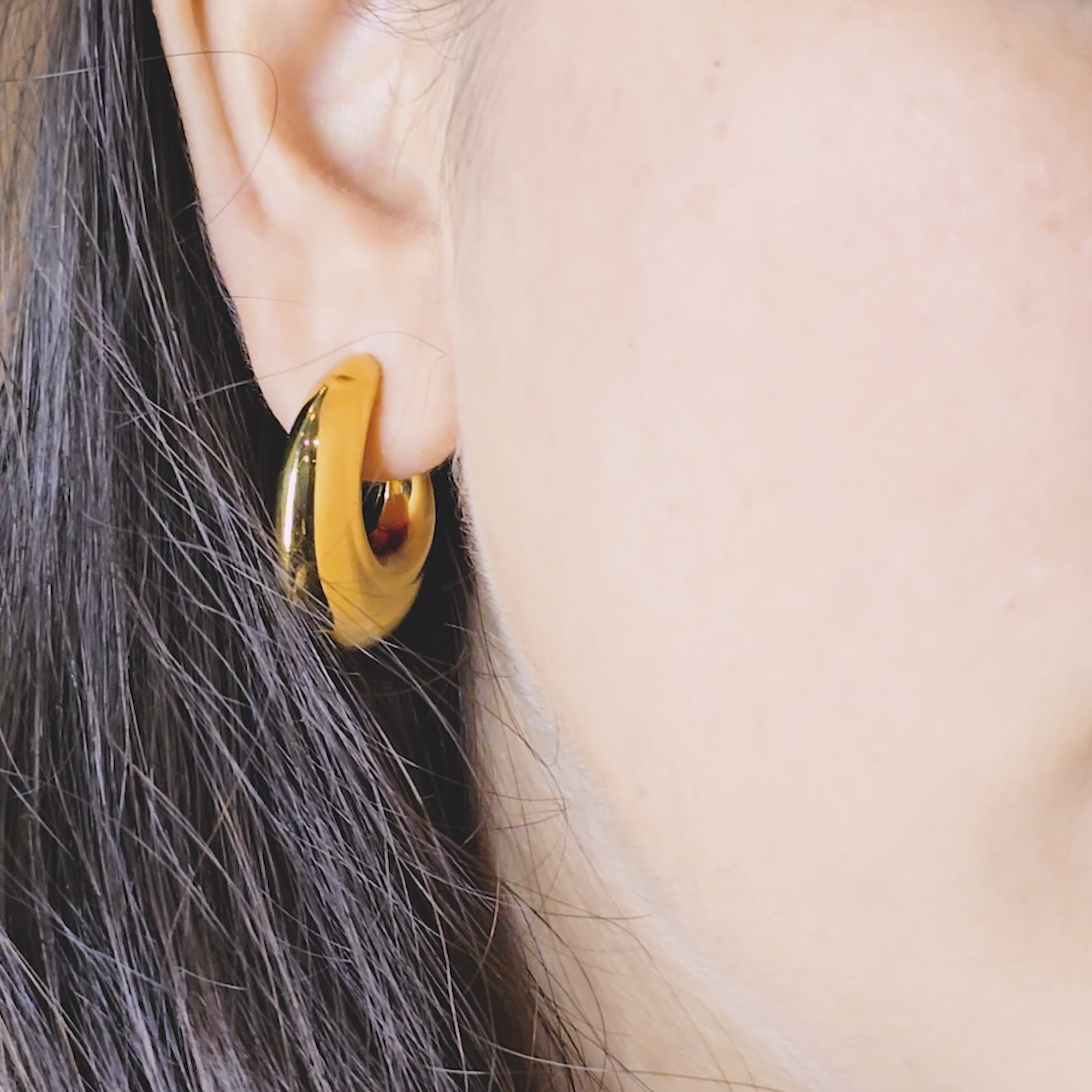 Model wearing Bold Loop Earrings—sculptural gold-toned hoops with a glossy finish, close-up side view.