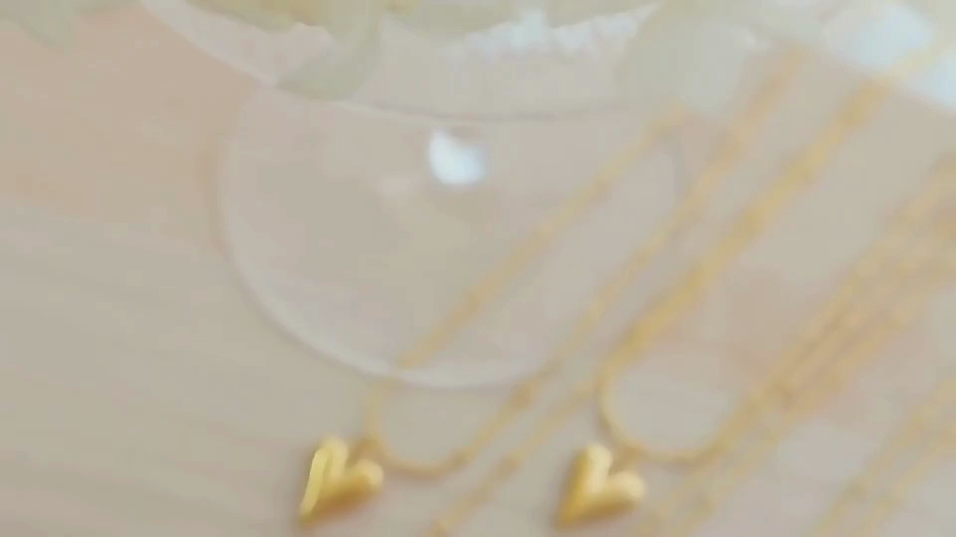 Close-up video of a gold-toned water drop heart pendant necklace with beaded chain, showcased in elegant lighting to highlight its shine and minimalist design