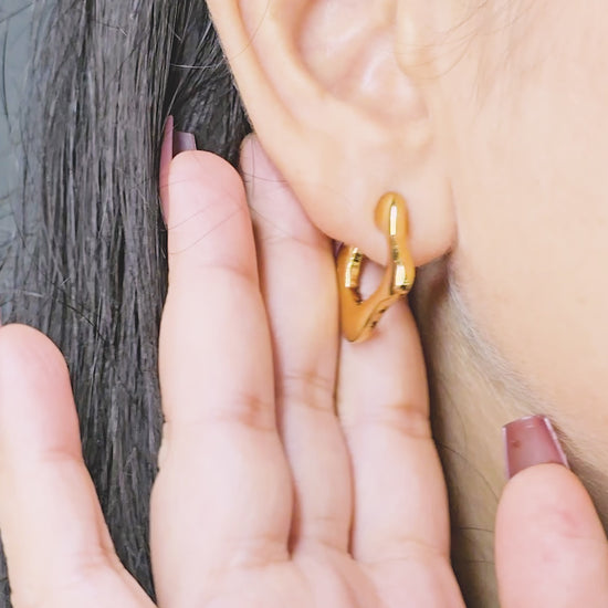 Close-up of model wearing Modern Melt Earrings – gold-toned abstract molten-style hoops – showcasing design details.