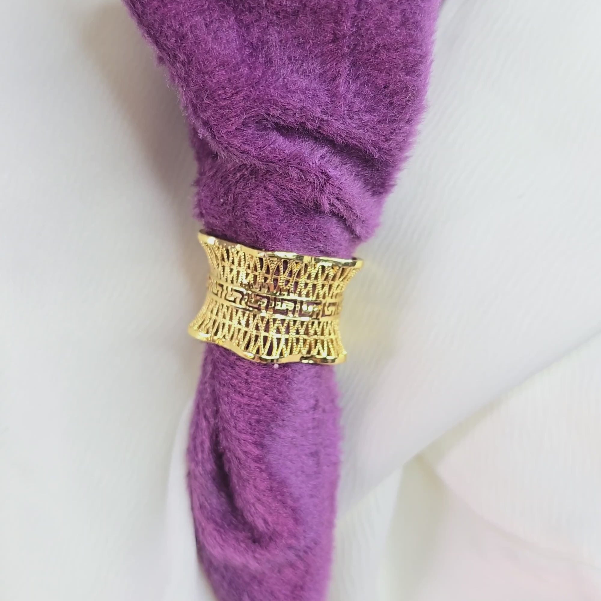 "360-degree video of the Empress Mesh Ring rotating on a display stand, showcasing its wide gold-toned band with intricate mesh texture and royal statement design, ring placed against a purple fabric background.
