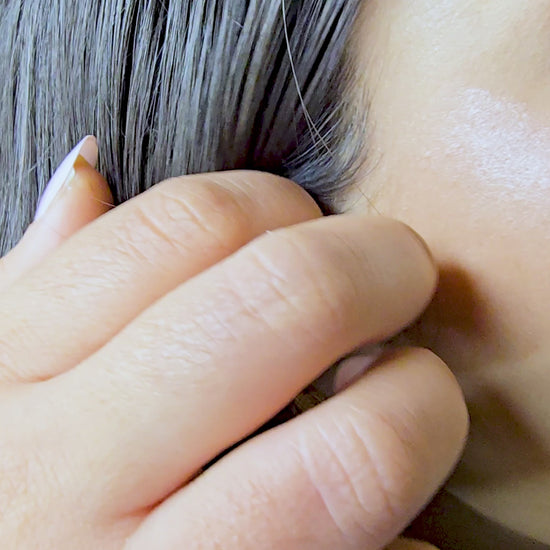 Video demonstration of the Zunari Charm Etched Heart Earring styled with the geometric hoop dangling from behind the earlobe. The model gently touches the earring to show how the anti-tarnish gold pieces layer together for a modern, three-dimensional look.