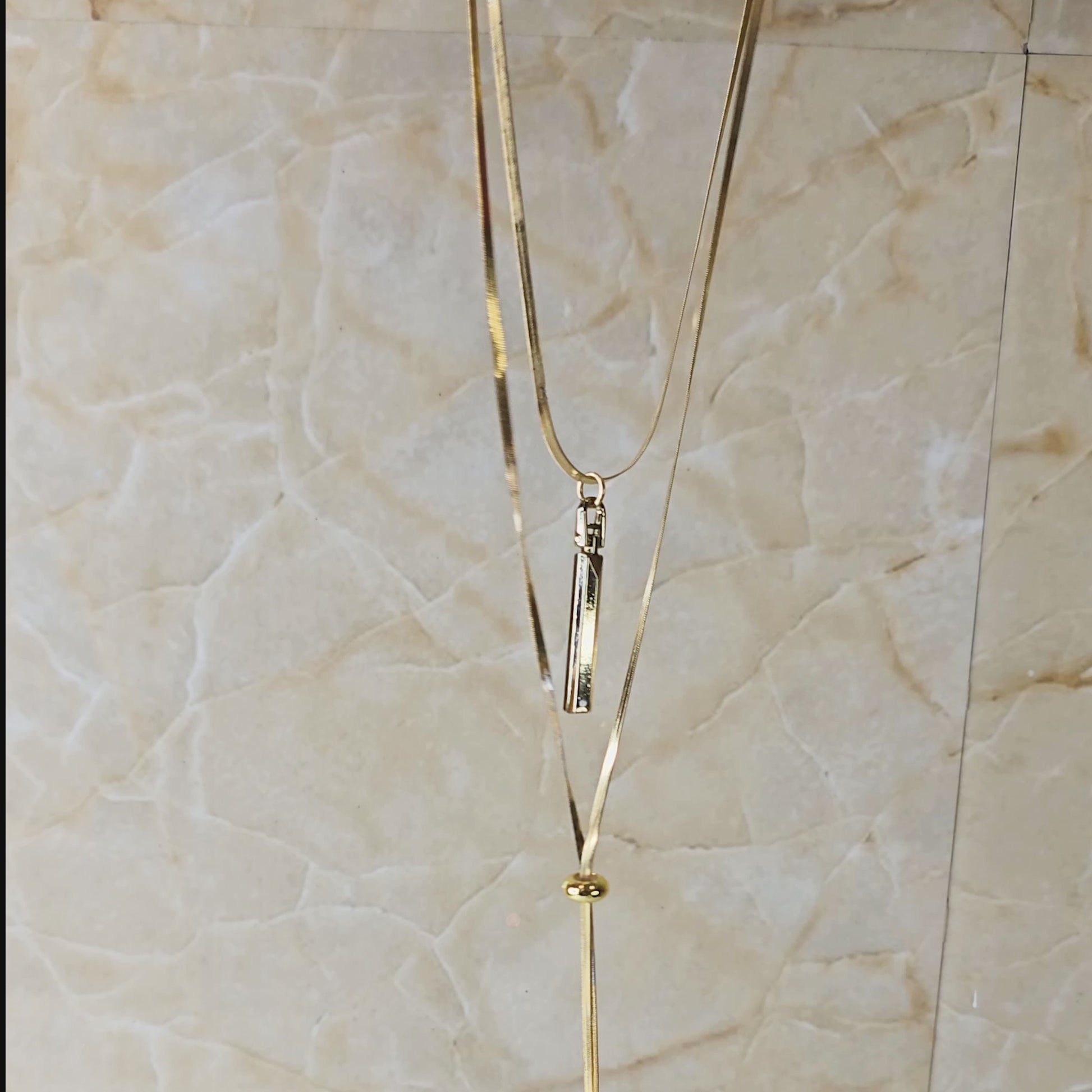 Video showing Layered Charm Drop Necklace from top to bottom, focusing on gold-toned layered chains, bar pendant, and coin drop charms with close-up detailing.