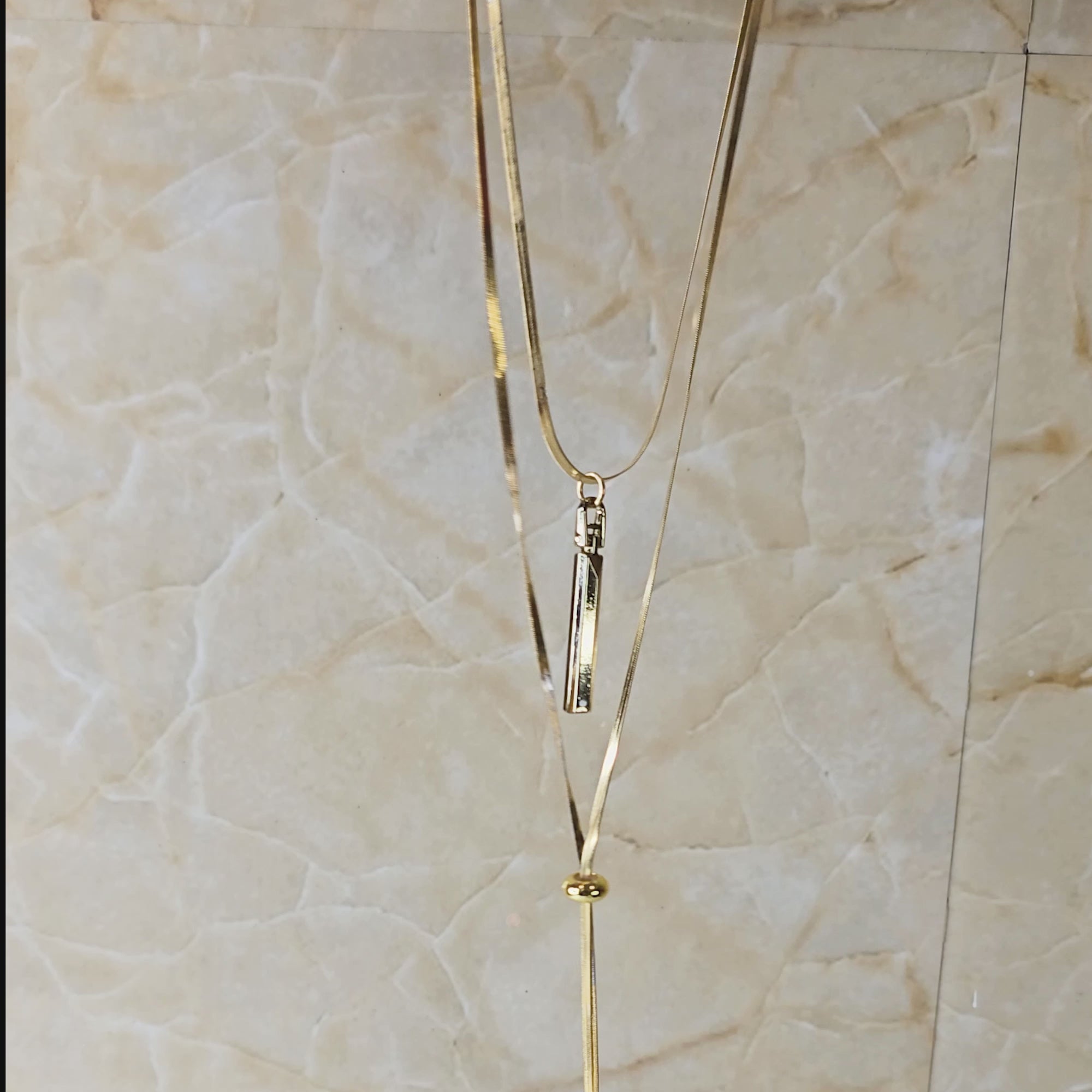 Video showing Layered Charm Drop Necklace from top to bottom, focusing on gold-toned layered chains, bar pendant, and coin drop charms with close-up detailing.